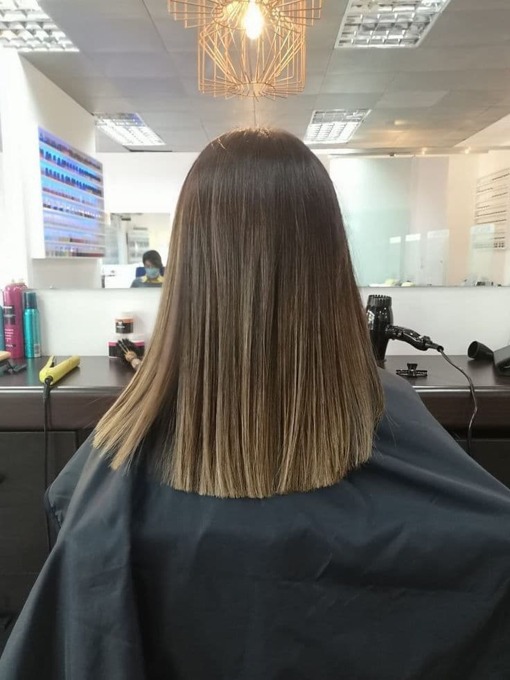 Cabello castaño liso con reflejos rubios y corte recto en un salón de belleza.