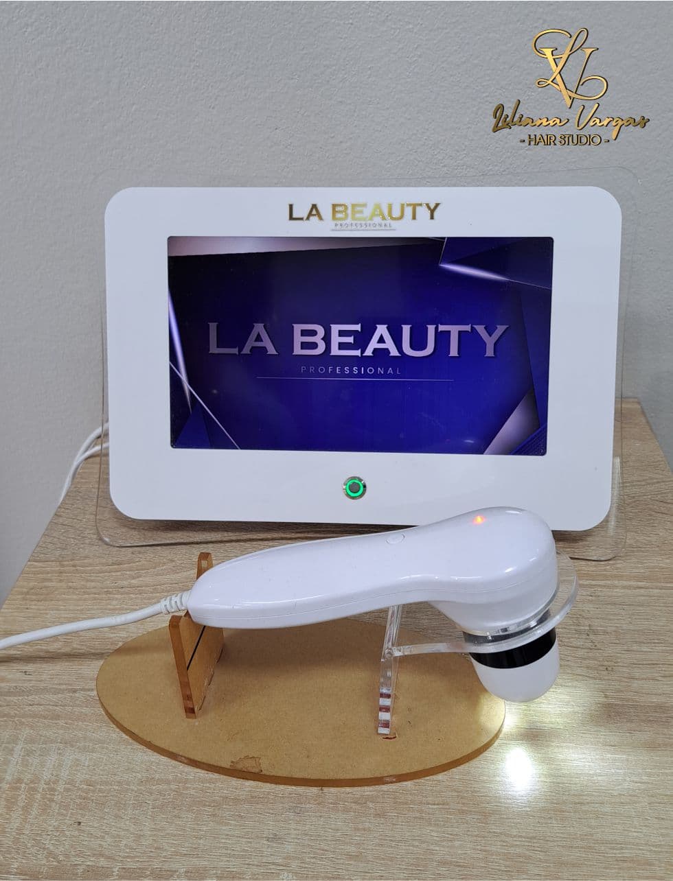 Dispositivo profesional LA BEAUTY con pantalla digital y aplicador manual blanco sobre un soporte.
